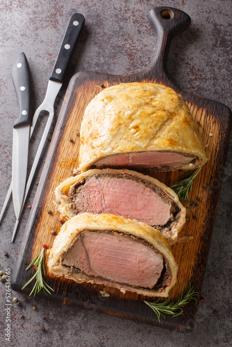 High angle beef wellington cooking or boeuf en crout cut into slices on a chopping board grey background. Vertical top view from above photo