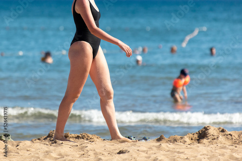 A girl in a bathing suit walks along the sandy beach