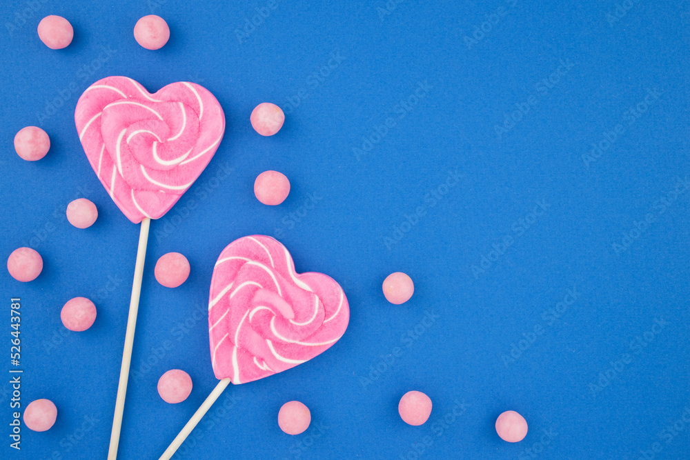 Lollipops and candies on a blue background. Dragees, sweets and sugar. Delicious pink hearts on a stick. Top view flat lay with copy space