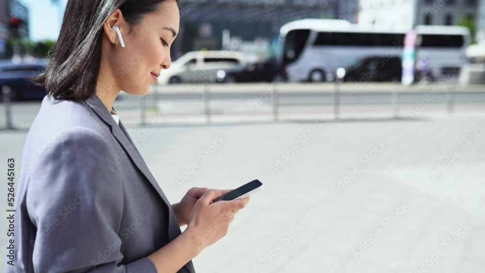 Young Asian business woman wearing suit using smartphone walking in big city on street outdoor. Korean lady professional executive typing on cellular phone, online mobile technology business apps tech