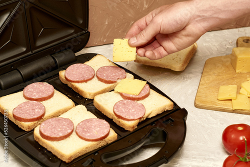 a man cooking sandwiches in a sandwich maker lays out pieces of cheese on bread