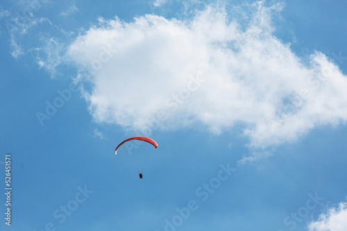 Red paraglider tandem instructor with a tourist flying into the sky with clouds on a sunny day