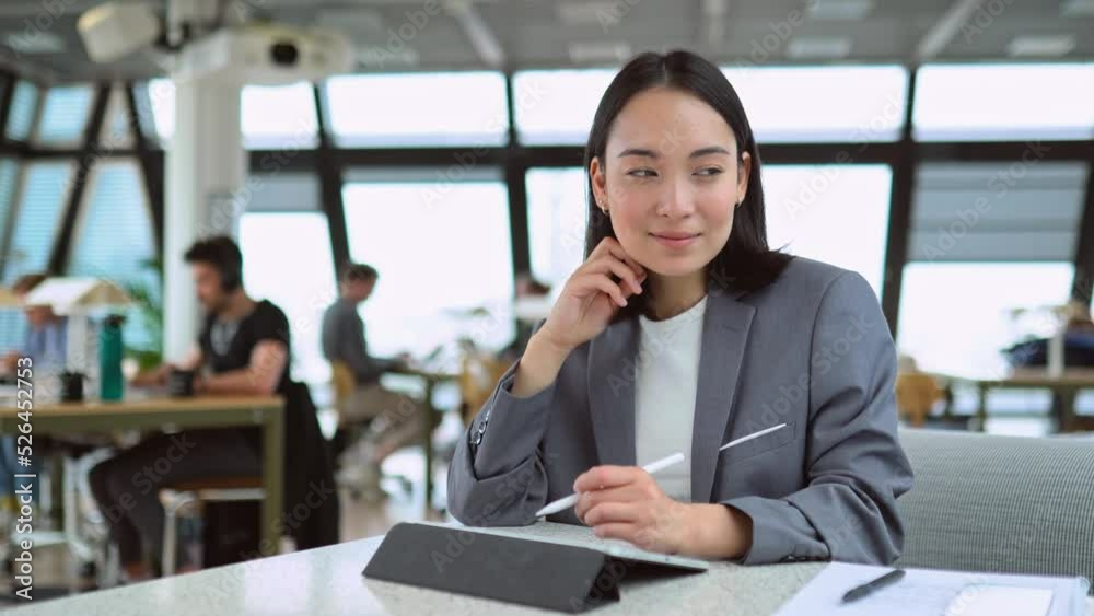 Busy young professional Asian business woman wearing suit using digital tablet learning online holding stylus writing e signature, doing online management working in big modern coworking office space. Busy young professional Asian business woman wearing suit using digital tablet learning online holding stylus writing e signature, doing online management working in big modern coworking office space.