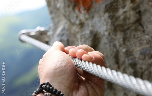 hand holding the steel rope of a via ferrata in the mountains during the hike photo
