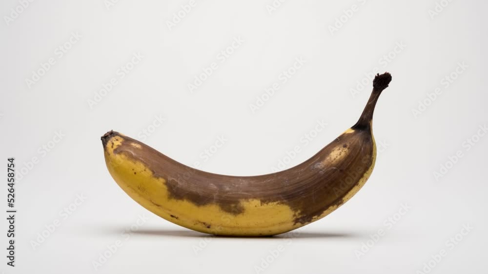 Ripening and decaying timelapse footage of a banana on a white background with a soft shadow.