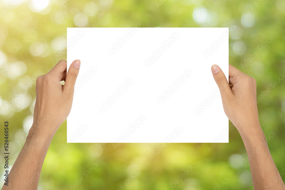Man holding empty paper with copy space in hands on green nature background. Man holding empty paper with copy space in hands on green nature background.