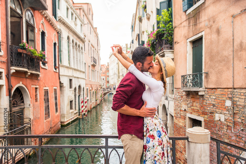 Happy beautiful couple of lovers doing romantic trip in Venice, Italy - Tourists visiting historic town of Venice and kissing in a traditional narrow street canal © oneinchpunch