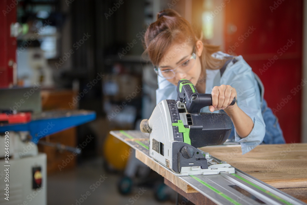 A female carpenter uses a chainsaw while working in a wood shop.