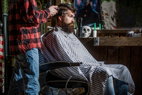 Hands of barber with hair clipper. Bearded man in barbershop. Haircut concept. Man visiting hairstylist in barbershop. Barber works with hair clipper. Hipster client getting haircut photo