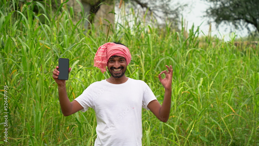 Young indian farmer showing smartphone screen at agriculture field ...