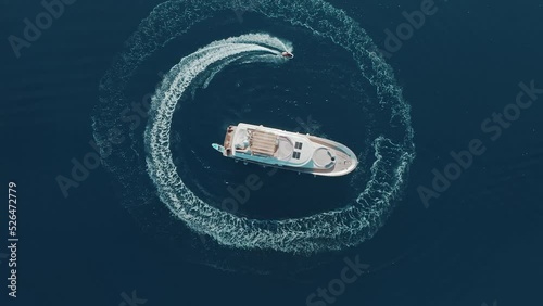 Young adventurous man with electric surfboard hydrofoil going around his luxury yacht in the circle and making beautiful shapes in the clear ocean. Hot summer day, enjoying water sport. Luxury holiday