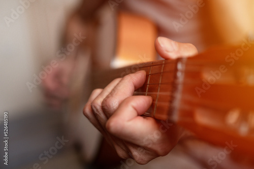 male hands of an elderly senior caucasian man holding and playing a classical guitar close up at home. unprofessional faceless guitarist people play amateur music. domestic hobbies and leisure. flare
