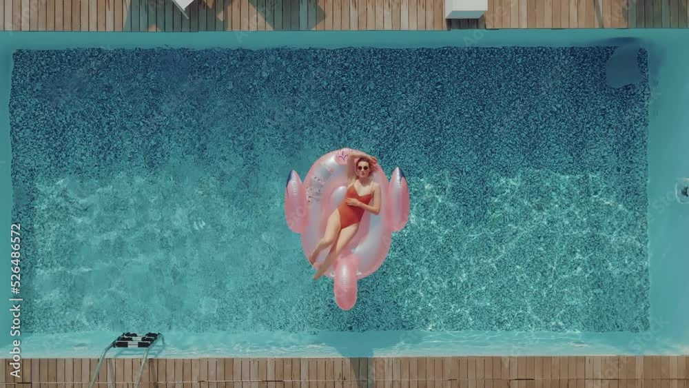 A young woman on vacation is laying on an inflatable pink flamingo in the middle of a swimming pool. Girl relaxing sunbathing enjoying travel holidays at resort pool in bikini. 