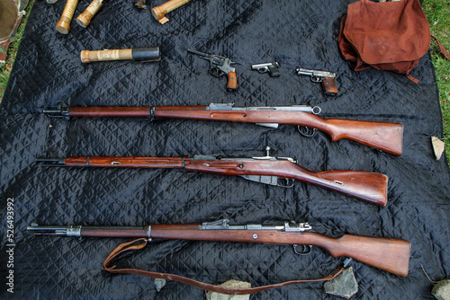 Several old rifles, guns and grenades aligned on the ground. 