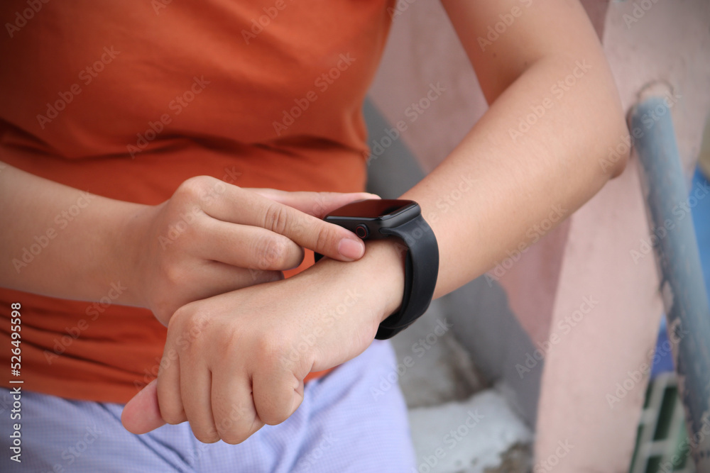 Fototapeta premium Women sitting on the grandstand raise hand and use finger to adjust setting application in smartwatch on wrist to checking result after workout or exercise. Concept of good health care.