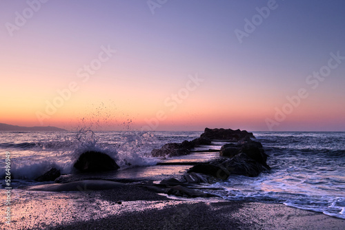eautiful sea and waves crashing against a jetty or pier at sunset time