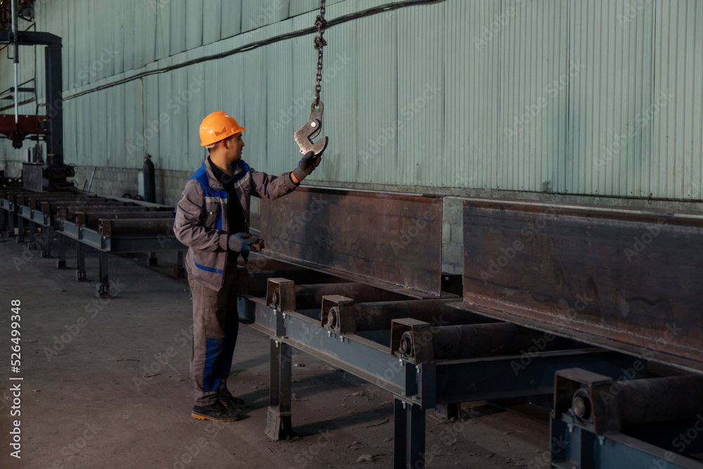 Worker receiving a metal bar from crane in warehouse
