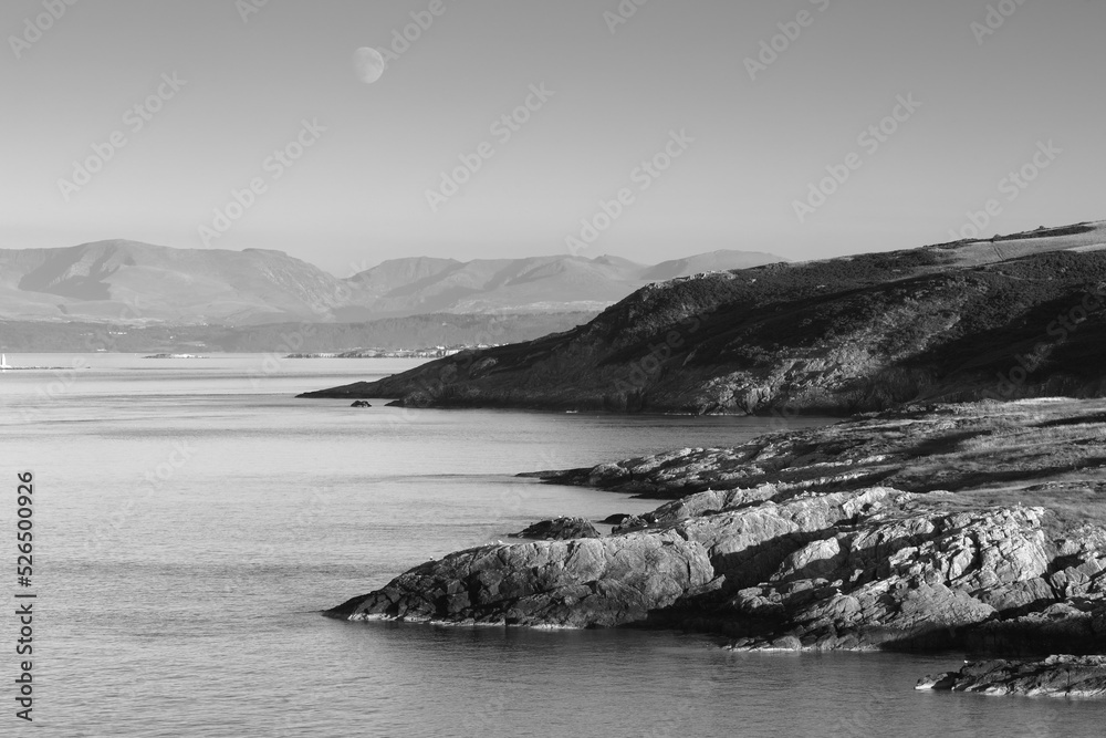 Black and white View from Point Lynas looking toward Snowdonia with the Moon rising. Anglesey, North Wales, UK.