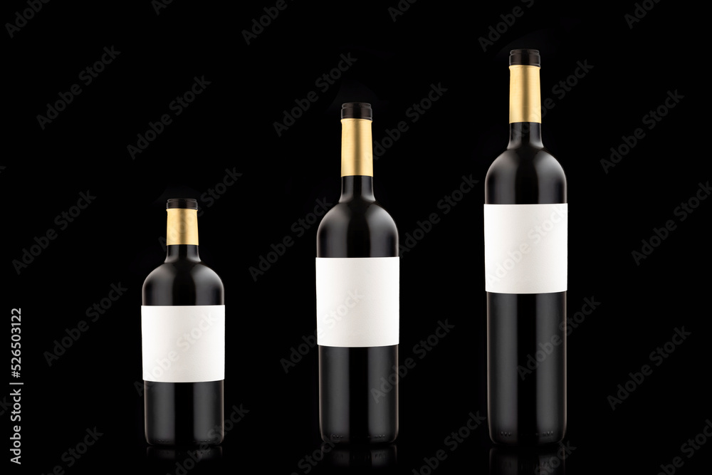 Three bottles of red wine with empty labels of different volume and size on a black background. Three bottles of red wine with empty labels of different volume and size on a black background.