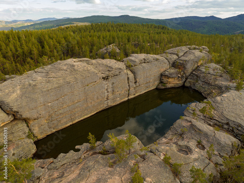 Lake Pool is the tetragonal stone bath surrounded by pine forest. Karkaraly National Park, Kazakhstan. Aerial top view.