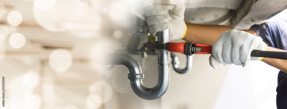 Plumber fixing white sink pipe with adjustable wrench.