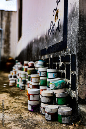 Many different colors used old oil paint bottles with worn out stickers of a traditional chinese calligraphy painter artist stacked on top of each other near the wall
