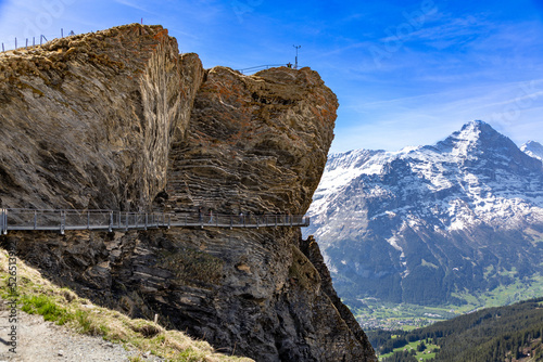 Walkway suspended from a rocky mountainside at First mountain near Grindelwald in the Swiss alps. Snow covered mountains in the background.  