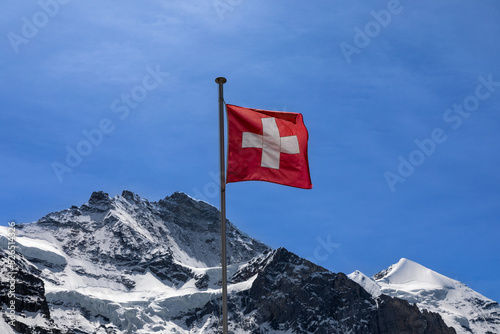 Flag of Switzerland with the top of the Jungfrau mountain behind it. 