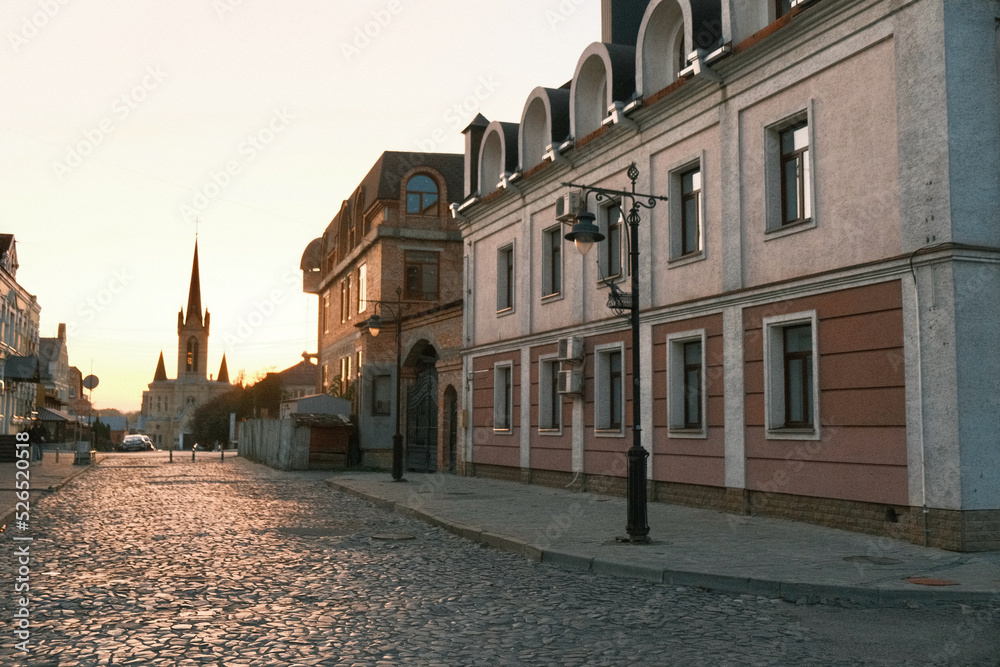 A beautiful ancient street with paving stones, beautiful buildings, vintage lampposts and a church in the background. Sunset on a beautiful street.