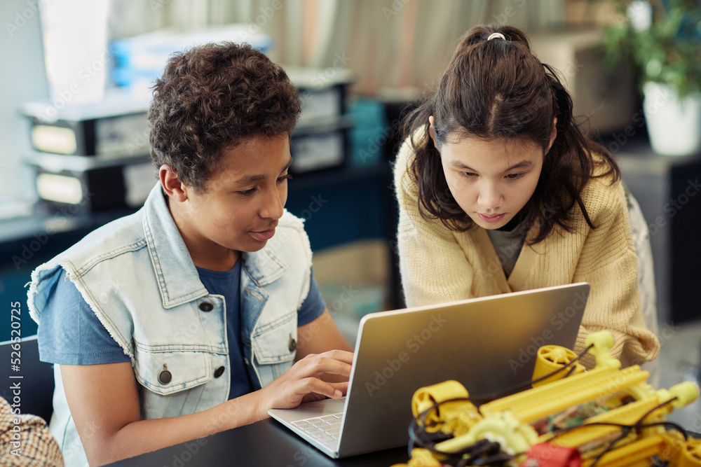Portrait of boy and girl using laptop together and programming robots during engineering class at school Portrait of boy and girl using laptop together and programming robots during engineering class at school