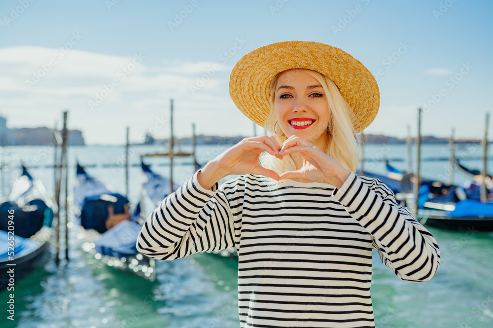Happy smiling traveler woman wearing straw hat, striped t-shirt, posing on the pier of Grand canal with gondolas in Venice, Italy.  Travel, vacation, lifestyle conception. Copy, empty space for text