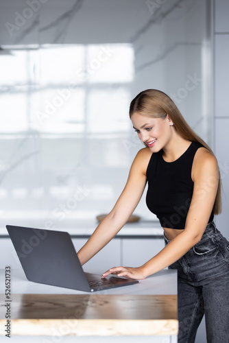 Smiling young woman typing on her laptop at kitchen