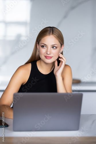 Beautiful woman drinking tea while working with laptop in cozy kitchen