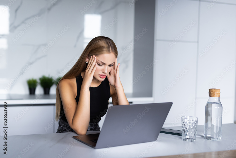 Concerned young woman thinking over domestic paperwork, sitting at laptop computer, papers, calculator at home, touching face, head, analyzing bills, taxes, expenses, financial problems
