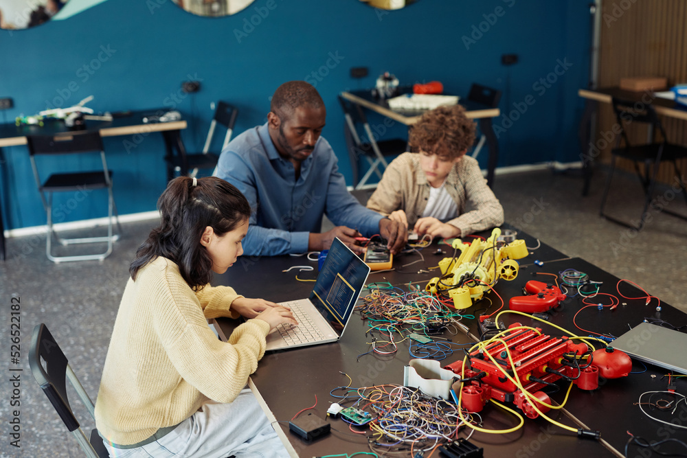 High angle portrait of young girl using laptop in engineering class and programming robots, copy space High angle portrait of young girl using laptop in engineering class and programming robots, copy space