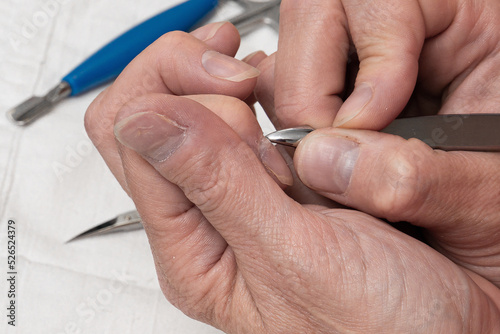 A woman makes herself a manicure, removes the cuticle skin on her nails with a metal device, takes care of her nails. Preparing the cuticle for cleaning and trimming. Top view very close up.