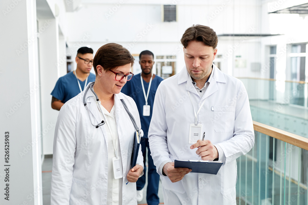 Waist up portrait of group of doctors holding clipboards while walking in hall of modern clinic