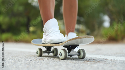 Close-up of female legs in rag sneakers on a longboard on the background of asphalt at sunset.