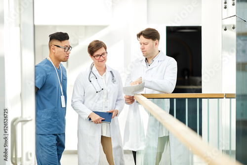 Group of expert doctors discussing case in hall of modern clinic in white tones, copy space