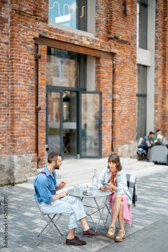 Stylish couple of colleagues have a conversation while sitting at cafe terrace in modern office district. Couple spending time together drinking water by the table outdoors