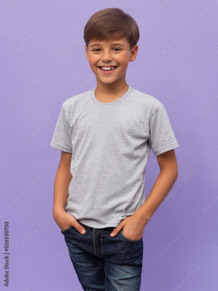 Self assured child in casual clothes and socks holding hands in pockets and looking at camera against lilac background