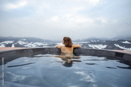 Young woman bathing in hot tub at mountains during winter. Concept of rest and recovery in hot vat on nature. Idea of escape and recreation on mountains
