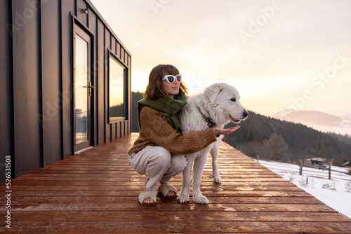Canvas Print Woman hugs her dog while resting on terrace of tiny house in the mountains on winter time