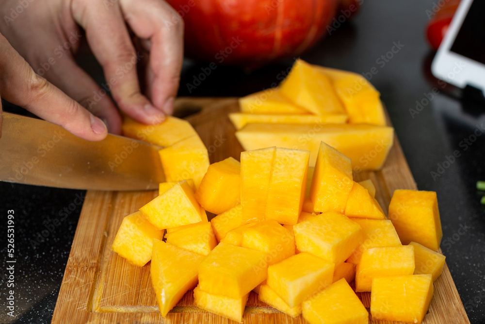 A man cooks food at home in the kitchen for the family, cuts a pumpkin on a cutting board A man cooks food at home in the kitchen for the family, cuts a pumpkin on a cutting board