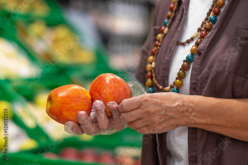 Female hands holding red apples in a supermarket or grocery store close-up. Woman holds two apples fruit wearing protective gloves photo