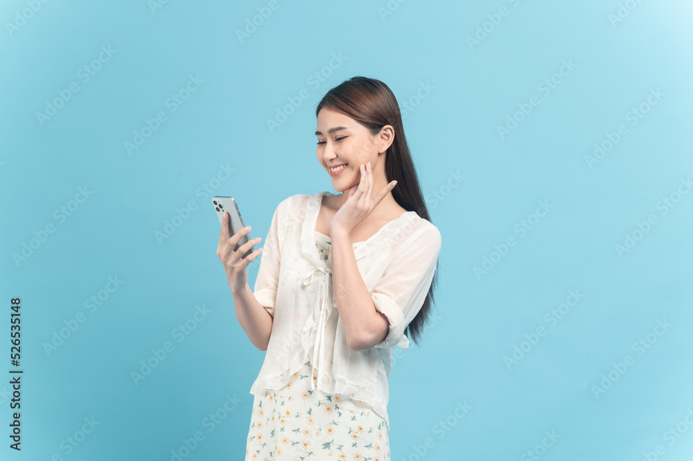 Beautiful young asian woman in white dress with flower pattern using smartphone isolated on blue background Beautiful young asian woman in white dress with flower pattern using smartphone isolated on blue background