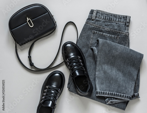Gray mom jeans, black leather sneakers and a cross body bag on a gray background, top view