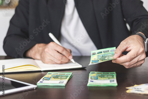 A man sits at his desk and counts money in euro cash.
