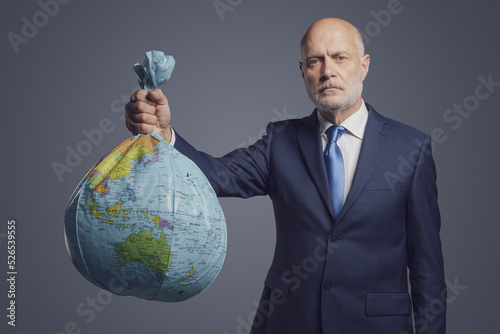 Businessman holding a polluted earth shaped as trash bag