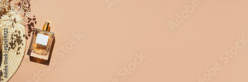 Transparent bottle of perfume with label. Cloth shopping bag and sun hat on beige background. Fragrance presentation with daylight. Trending concept in natural materials with yellow field flowers
